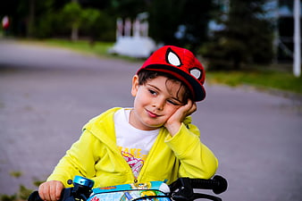 Tired young boy in Spider-Man hat resting on bicycle handlebars