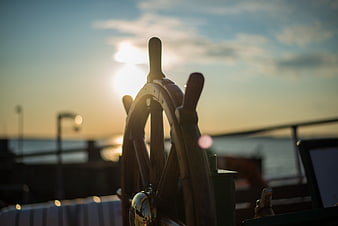 Wooden ship wheel silhouette against sunset ocean background