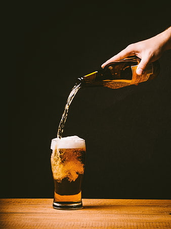 Hand Pouring Golden Beer into Glass on Wooden Table