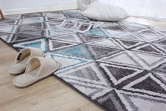 Geometric Patterned Area Rug With Slippers And Pillow On Wooden Floor