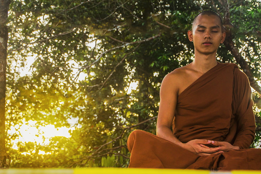 Young Buddhist Monk Meditating in Forest at Sunset
