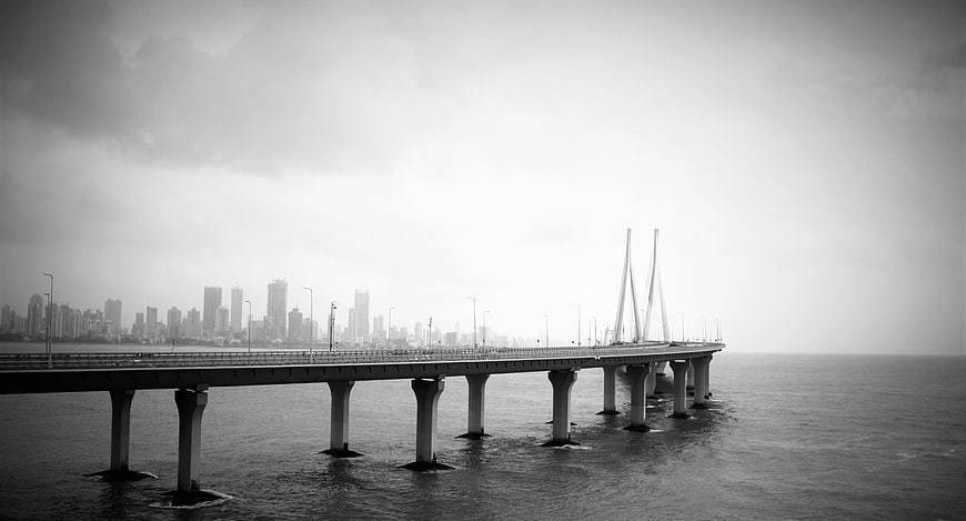 Black and white cable-stayed bridge over ocean with city skyline