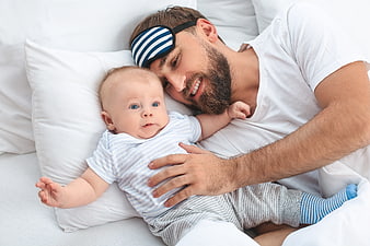 Happy Father with Sleep Mask Cuddling Baby in Bed