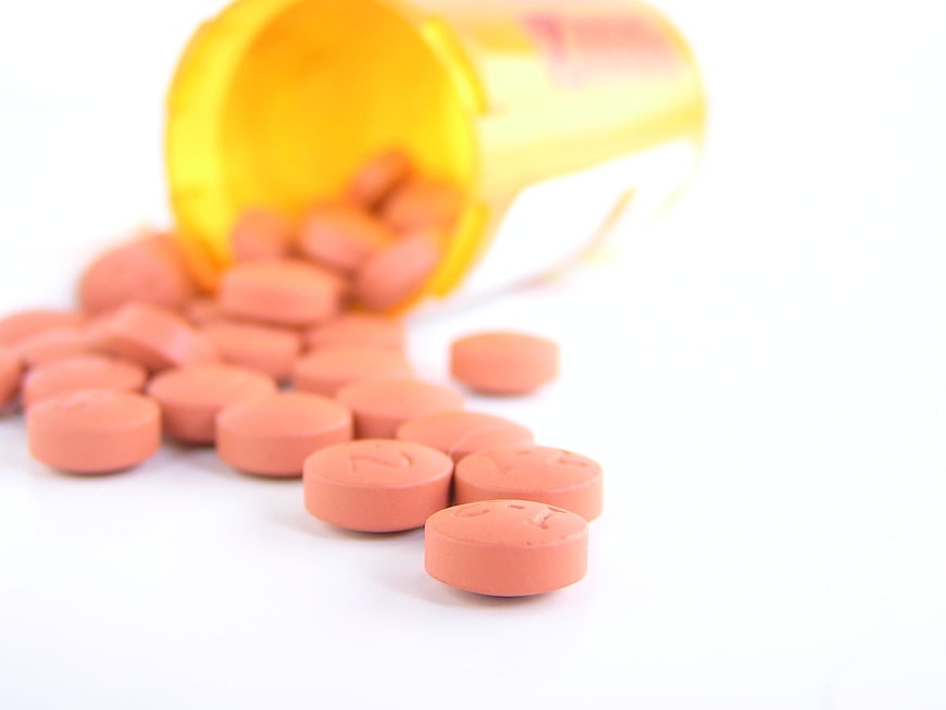 Orange prescription pills spilling from yellow bottle on white background