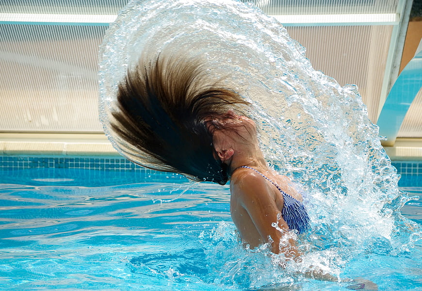 Woman splashing water in swimming pool with flying hair