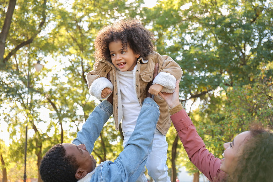 Happy family playing in park lifting child up