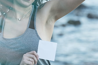 Woman holding blank card near clean armpit by the ocean