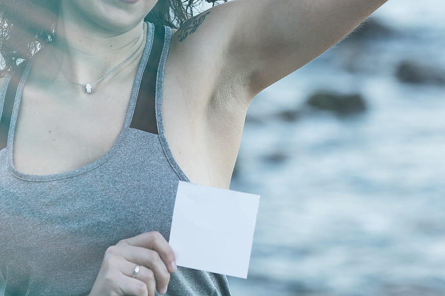 Woman holding blank card near clean armpit by the ocean