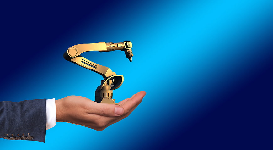 Businessman hand holding miniature golden robotic arm on blue background