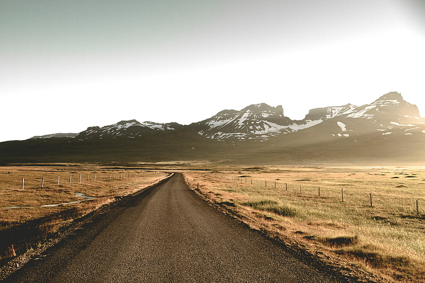 Paved road leading to snow-capped mountains in golden hour
