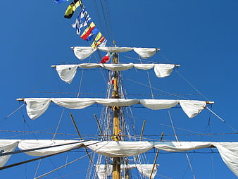 Tall ship mast with furled sails against blue sky