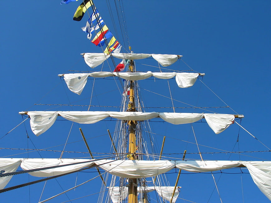 Tall ship mast with furled sails against blue sky