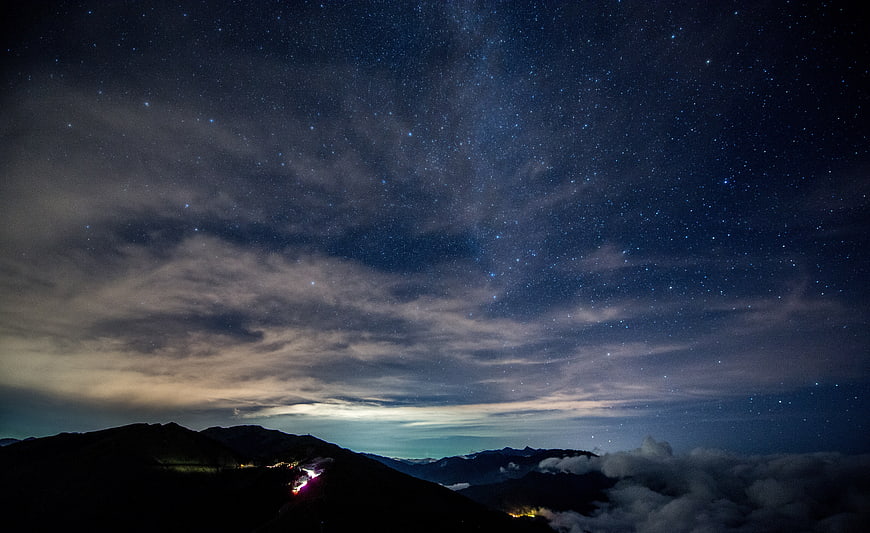 Starry night sky over mountain silhouette with clouds