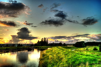 Dramatic sunset over a canal with vibrant green grass and clouds