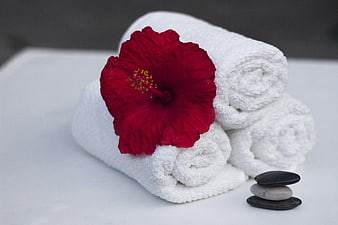 Rolled white towels with red hibiscus flower and stacked zen stones