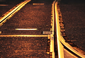 Close-up of train tracks on asphalt road at sunset