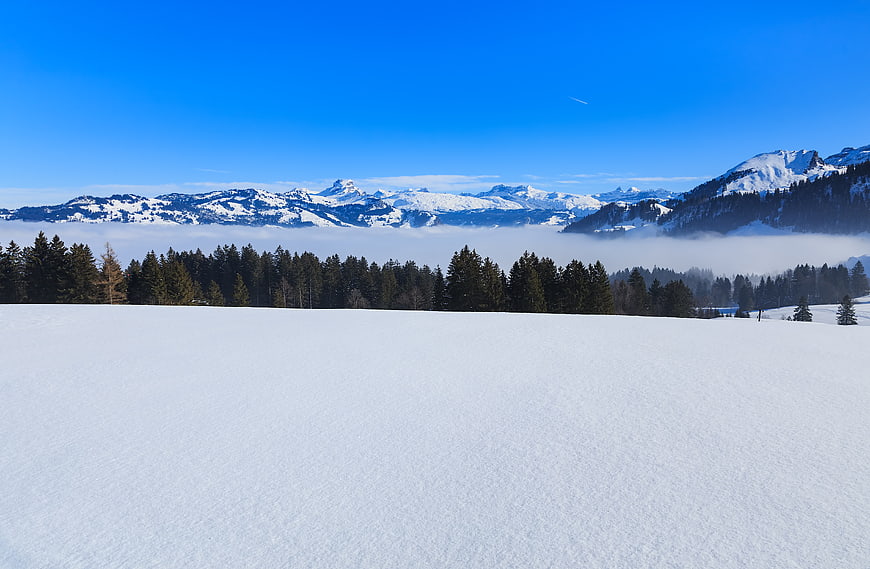 Snowy Winter Landscape with Mountain Range and Blue Sky