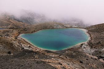 Turquoise volcanic crater lake in misty mountain landscape