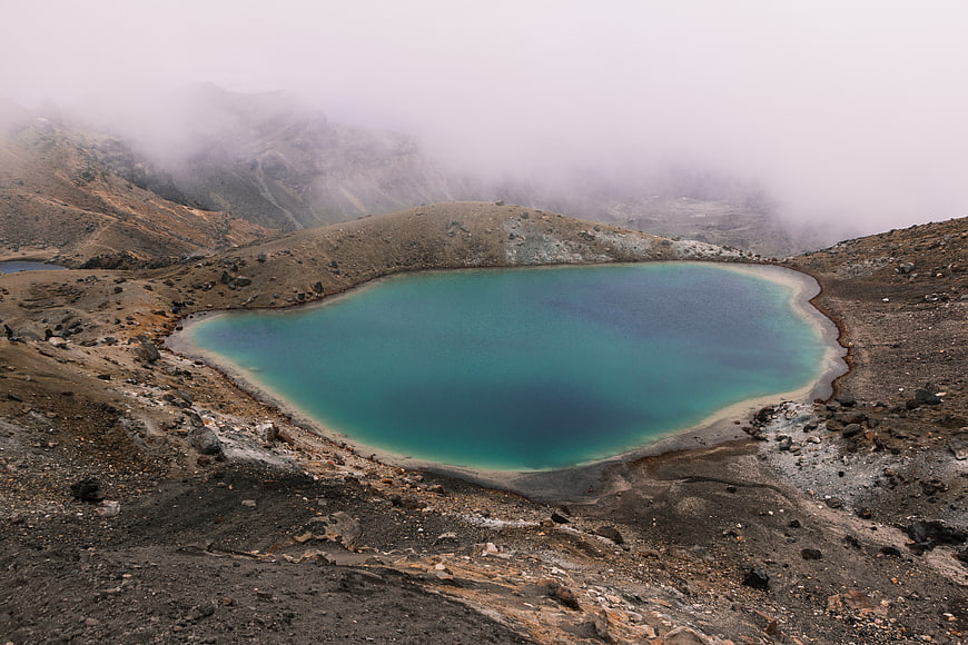 Turquoise volcanic crater lake in misty mountain landscape