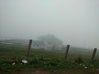 Misty house behind barbed wire fence in foggy field