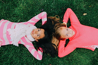 Two young girls lying on green grass looking up at camera