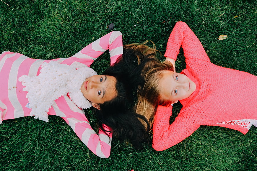 Two young girls lying on green grass looking up at camera