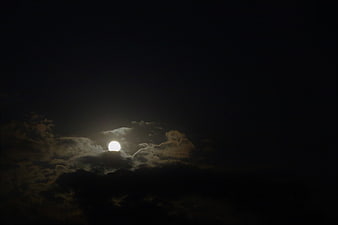 Full moon glowing through dark clouds at night