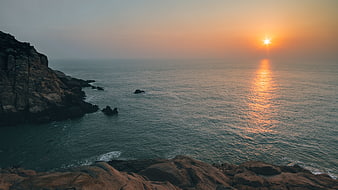 Sunset over rocky coastline with ocean waves and golden light