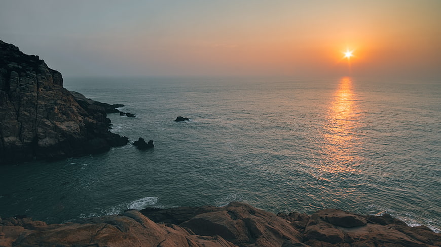 Sunset over rocky coastline with ocean waves and golden light