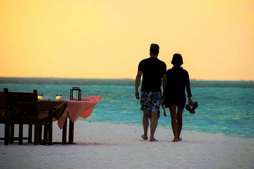 Couple walking on tropical beach at sunset with dining table