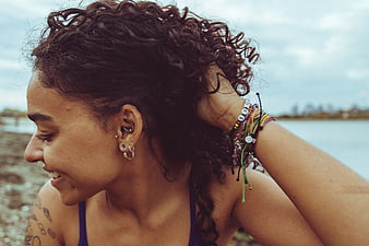 Smiling woman with curly hair and bracelets by the ocean