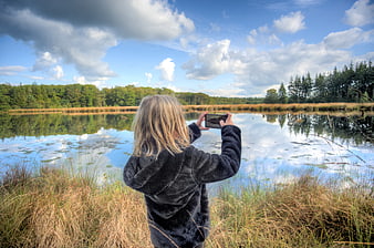 Child taking photo of lake with smartphone in nature