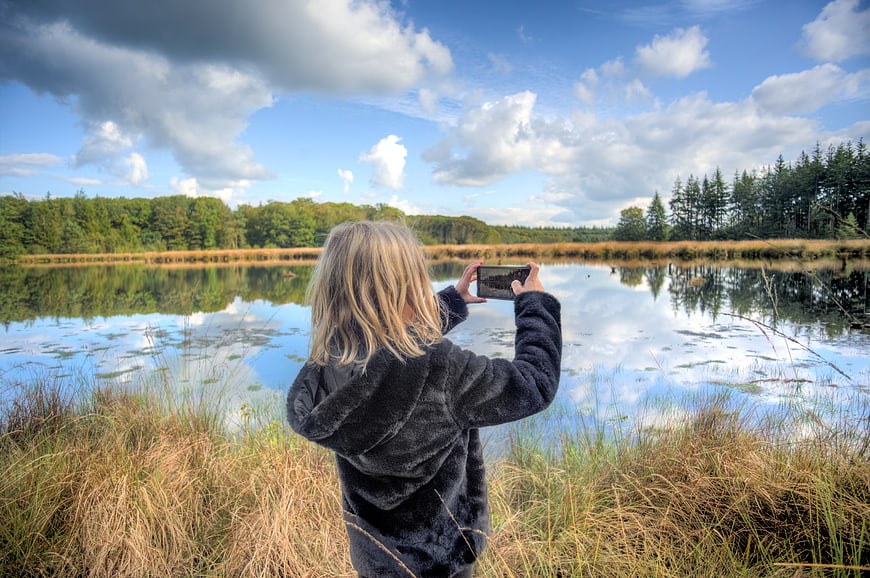 Child taking photo of lake with smartphone in nature
