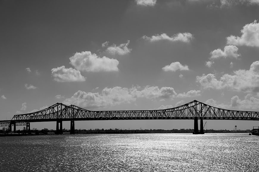 Black and white steel truss bridge over river with clouds