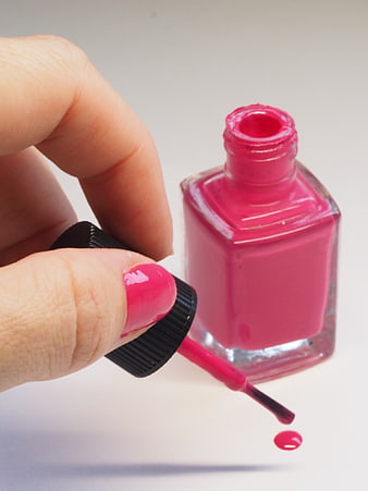 Close-up of pink nail polish bottle and painted fingernail