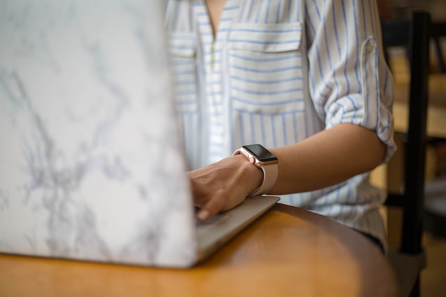 Woman Typing on Laptop with Smartwatch at Wooden Table