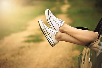 Relaxed legs in white sneakers hanging from car window
