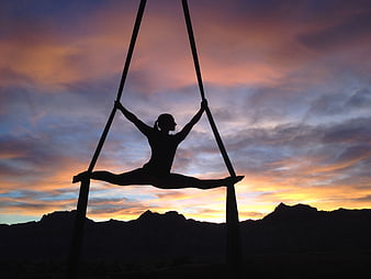 Silhouette of female aerialist performing split on silks at sunset