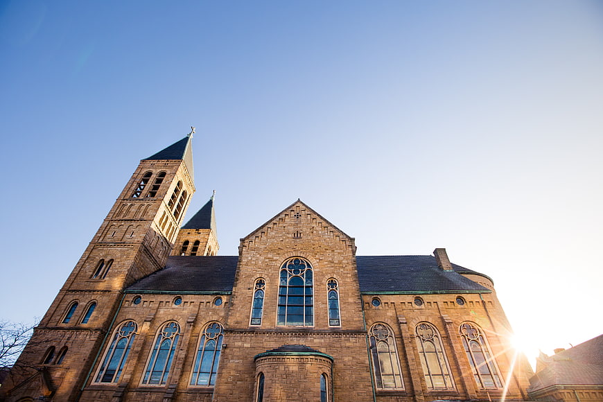 Low angle view of historic brick church with twin spires against blue sky