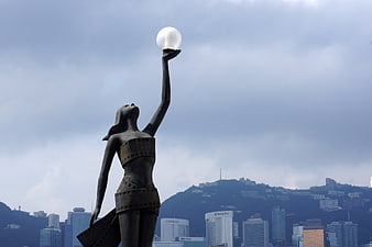 Statue of woman holding sphere against Hong Kong city skyline