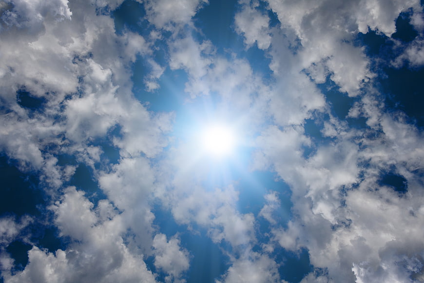 Sun shining through scattered cumulus clouds in blue sky