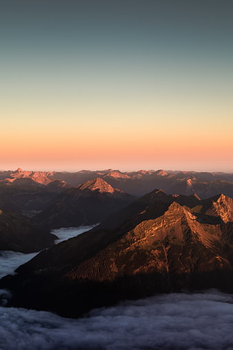 Alpine mountain peaks above clouds at golden hour sunrise