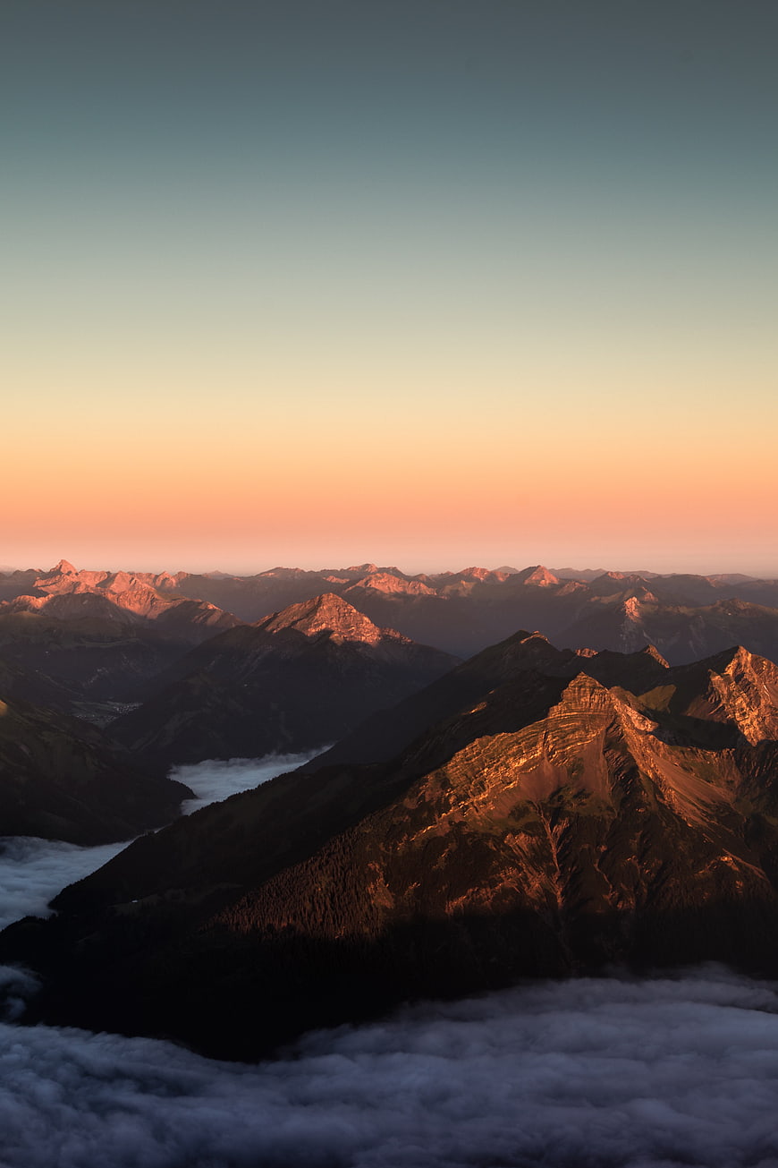 Alpine mountain peaks above clouds at golden hour sunrise