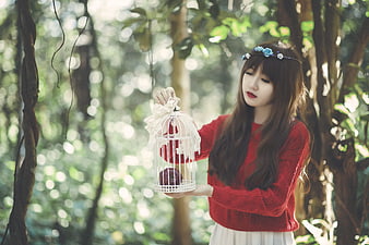 Woman in Red Sweater Holding White Birdcage in Forest