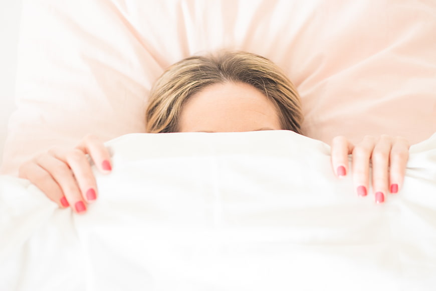 Woman Hiding Under White Bed Covers with Pink Nails