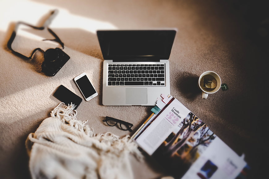 Flat lay of laptop, camera, and coffee on beige carpet