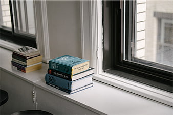 Stacks of books on a white windowsill near a window