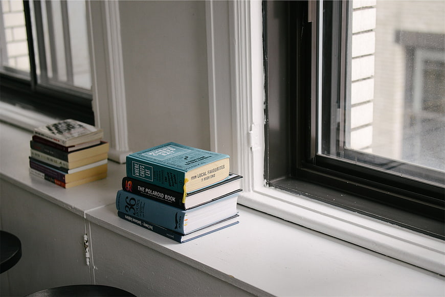 Stacks of books on a white windowsill near a window