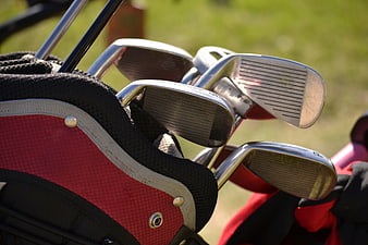 Close-up of golf clubs in a red bag on a sunny course