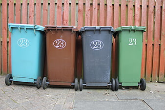 Four colored recycling bins lined up against a wooden fence